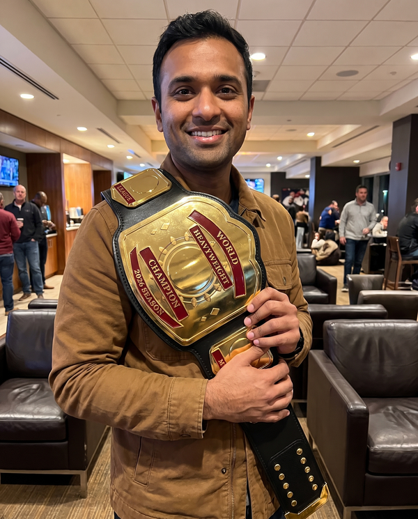 Man in a sports lounge holding a Zees Belts CrownForge custom championship belt engraved World Heavyweight Champion 2026 Season